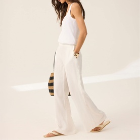 Model wearing Mint Velvet Scalloped Trim High-Rise Linen Trousers in white, styled with a white vest top and tan flat sandals.