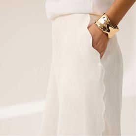 Model wearing Mint Velvet White Scalloped Trim High-Rise Linen Trousers, styled with a white top and gold cuff bracelet.