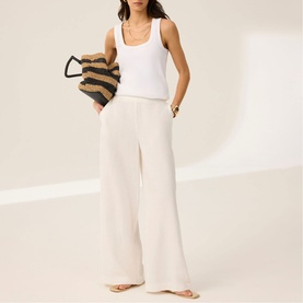 Model wearing Mint Velvet White Scalloped Trim High-Rise Linen Trousers with a white vest top, carrying a striped tote bag.