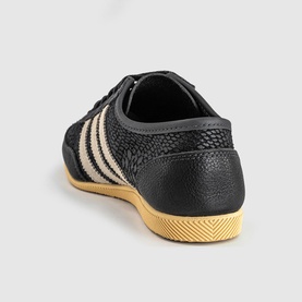 Adidas trainer in utility black with cream white three stripes, textured upper, and honey gum sole, rear angle view.