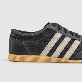 Adidas trainer in utility black with cream white three stripes, textured upper, dark laces, and gum rubber sole.