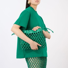 Model carrying The Frankie Shop Morgan Leather Clutch Bag in emerald, knotted mesh design with drawstring, styled with matching green top and skirt