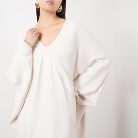Model wearing The Frankie Shop ivory viscose dress with V-neckline and oversized batwing sleeves, styled with gold drop earrings.