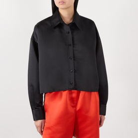 Model wearing The Frankie Shop black satin oversized shirt with cropped hem, styled with red wide-leg trousers.