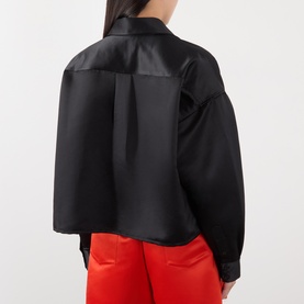 Model wearing The Frankie Shop black satin shirt, rear view, cropped silhouette with box pleat, styled with red trousers.
