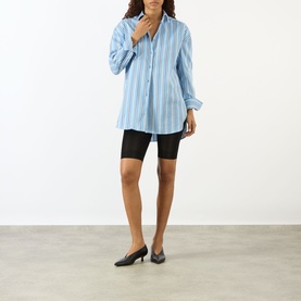 Model wearing The Frankie Shop Oana Padded Stripe Shirt in Blue Multi Stripe, styled with black cycling shorts and black kitten heels.