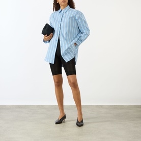 Model wearing The Frankie Shop Oana Padded Stripe Shirt in Blue Multi Stripe, styled with black cycle shorts, clutch bag and black heels.