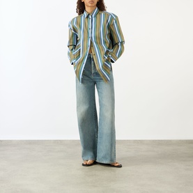 Model wearing The Frankie Shop Oana Padded Stripe Shirt in Green Multi Stripe with wide-leg light-wash jeans and flat sandals.