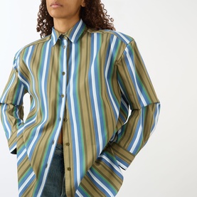Model wearing The Frankie Shop Oana Padded Stripe Shirt in Green Multi Stripe, showing long sleeves and dropped shoulders, styled with blue jeans.