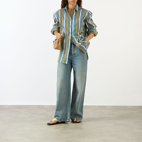 Model wearing The Frankie Shop Oana Padded Stripe Shirt in Green Multi Stripe with wide-leg jeans and sandals, carrying a small tan bag.