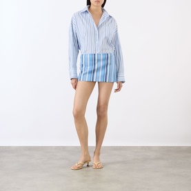 Model wearing The Frankie Shop Blue Multi Stripe mini skirt, styled with matching striped shirt and gold flat sandals.