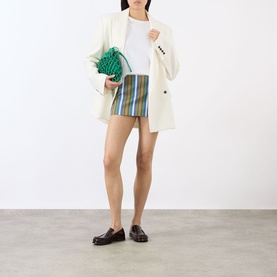 Model wearing The Frankie Shop Green Multi Stripe mini skirt, styled with white blazer, white tee and dark loafers, carrying green woven clutch bag.
