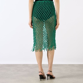 Model wearing The Frankie Shop green leather macram&eacute; midi skirt with fringe hem, styled with black strappy heels, rear view