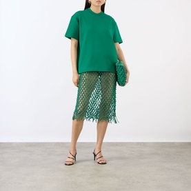 Model wearing The Frankie Shop green leather mesh fringed midi skirt, styled with matching green top and clutch bag, black strappy heels.