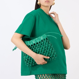 Model wearing The Frankie Shop Emerald T-shirt in cotton blend, styled with a green netted clutch bag and matching skirt.