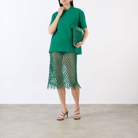 Model wearing The Frankie Shop Emerald T-shirt, styled with matching green mesh fringed skirt and black strappy heels, carrying green clutch bag.