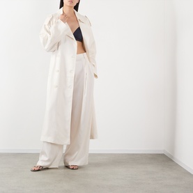 Model wearing The Frankie Shop ivory silk wide-leg trousers, styled with a matching longline coat and dark bralet.