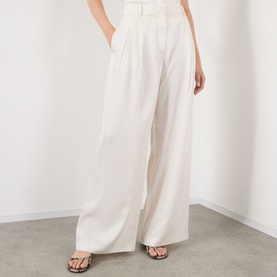 Model wearing The Frankie Shop ivory wide-leg silk trousers with high waist and front pleats, styled with brown strappy flat sandals.