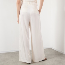 Model wearing The Frankie Shop ivory wide-leg silk trousers, rear view, styled with strappy sandals.