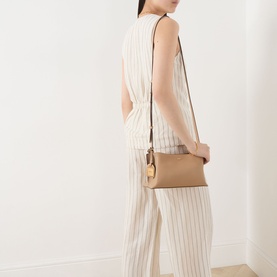 Model carrying DKNY Ayla Crossbody Bag in cappuccino with gold-toned hardware and adjustable strap, styled with striped wide-leg trousers