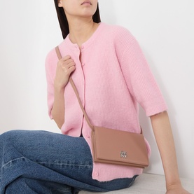 Model carrying DKNY Etta Wallet Crossbody Bag in Hot Cocoa pebbled finish with silver-tone hardware, worn on adjustable strap over pink cardigan