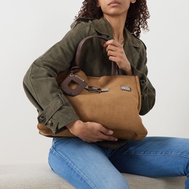 Model carrying DKNY Bryar Large Satchel Bag in almond faux suede, silver-tone hardware, top handles and keyring detail, styled with olive jacket and