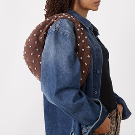 Model carrying DKNY Katya Studded Shoulder Bag in chocolate faux suede with silver-tone studs and fixed strap, styled over denim jacket