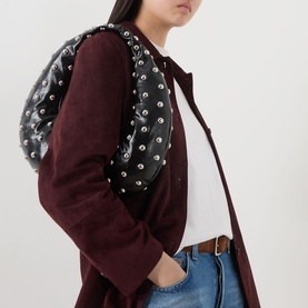 Model carrying a black studded backpack with silver hardware, styled with a burgundy coat and jeans