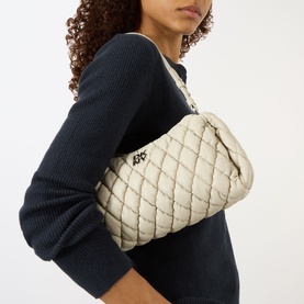 Model carrying DKNY Remy Quilted Shoulder Bag in light taupe with silver-tone hardware and quilted finish, styled with navy ribbed sweater