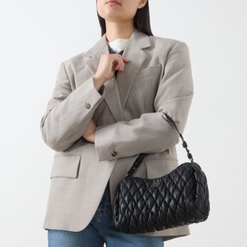Model carrying DKNY Remy Quilted Shoulder Bag in black with silver-tone hardware, styled with a grey blazer.