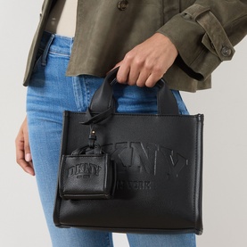 Model carrying DKNY Hadlee Small Tote Bag in black with embossed logo, gold-tone hardware, top handles and mini charm pouch