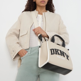 Model carrying DKNY Hadlee Small Tote Bag in light taupe with black trim, logo branding, top handles and gold-tone hardware, styled with sage trousers