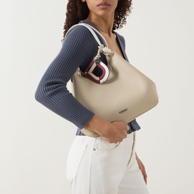 Model carrying DKNY Paula Medium Tote Bag in light taupe, silver-tone hardware, knotted top handles. Styled with blue ribbed top and white jeans.