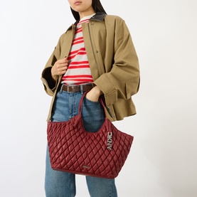 Model carrying DKNY Paula Quilted Medium Tote Bag in Rhythm Red with silver-tone hardware, styled with a khaki jacket and striped top.