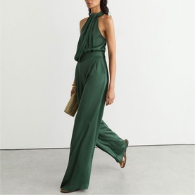 Model wearing Reiss teal green halterneck wide-leg jumpsuit, styled with gold strappy sandals and a woven clutch bag.