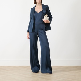 Model wearing navy satin wide-leg trousers and matching blazer, styled with a camisole top, carrying a small white clutch bag