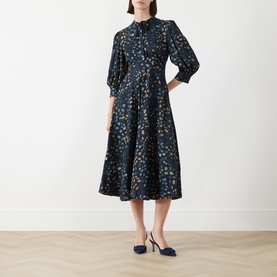 Model wearing Marella Navy Pebbles dress with puffed sleeves, floral print, and full midi skirt, styled with navy heels.