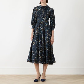 Model wearing Marella Navy Pebbles dress with floral print, three-quarter sleeves, high neck, and flared midi skirt, styled with navy heels.