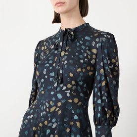 Model wearing Marella Navy Pebbles dress with tie neck, long sleeves and multicolour abstract pebble print on navy viscose fabric.