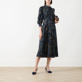 Model wearing Marella Navy Pebbles dress with blue and gold print, midi length, balloon sleeves, with navy slingback heels and tan belt.