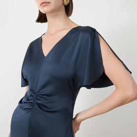 Model wearing Marella aviation blue satin dress with V-neck, split sleeves and ruched front detail, styled with gold hoop earrings.