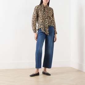 Model wearing Marella Nastro Silk Leopard Print Blouse in beige, with pussy bow tie, styled with blue wide-leg jeans and black flat mules.