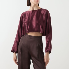 Model wearing Marella bordeaux cropped satin blouse with long sleeves and open back detail, styled with brown wide-leg trousers.