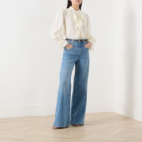 Model wearing Marella Caldaia Silk Ruffle Blouse in white with puff sleeves and ruffle front, styled with wide-leg blue jeans and strappy heels.