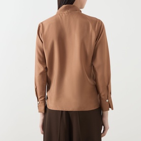 Model wearing Marella Kabala Silk Tie Front Blouse in Tobacco Brown, rear view showing buttoned cuffs and curved hem, styled with brown trousers