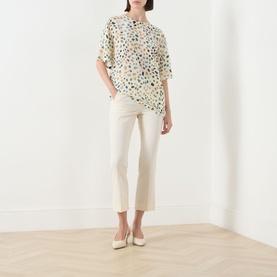 Model wearing Marella White Pebbles silk shirt with abstract print, styled with cream trousers and nude heels.