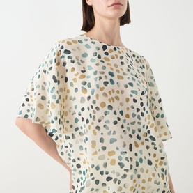 Model wearing Marella White Pebbles silk shirt with abstract stone print in teal, olive and gold tones, flutter sleeves visible.