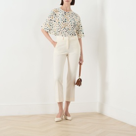 Model wearing Marella White Pebbles silk shirt with floral dot print, styled with cream cropped trousers, white flats and brown mini bag.