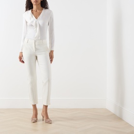 Model wearing Marella white slim-leg trousers, styled with a white tie-neck blouse and nude heels.