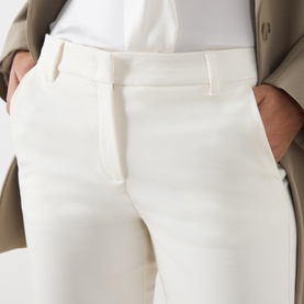 Model wearing Marella white tailored trousers with belt loops and side pockets, styled with a beige coat